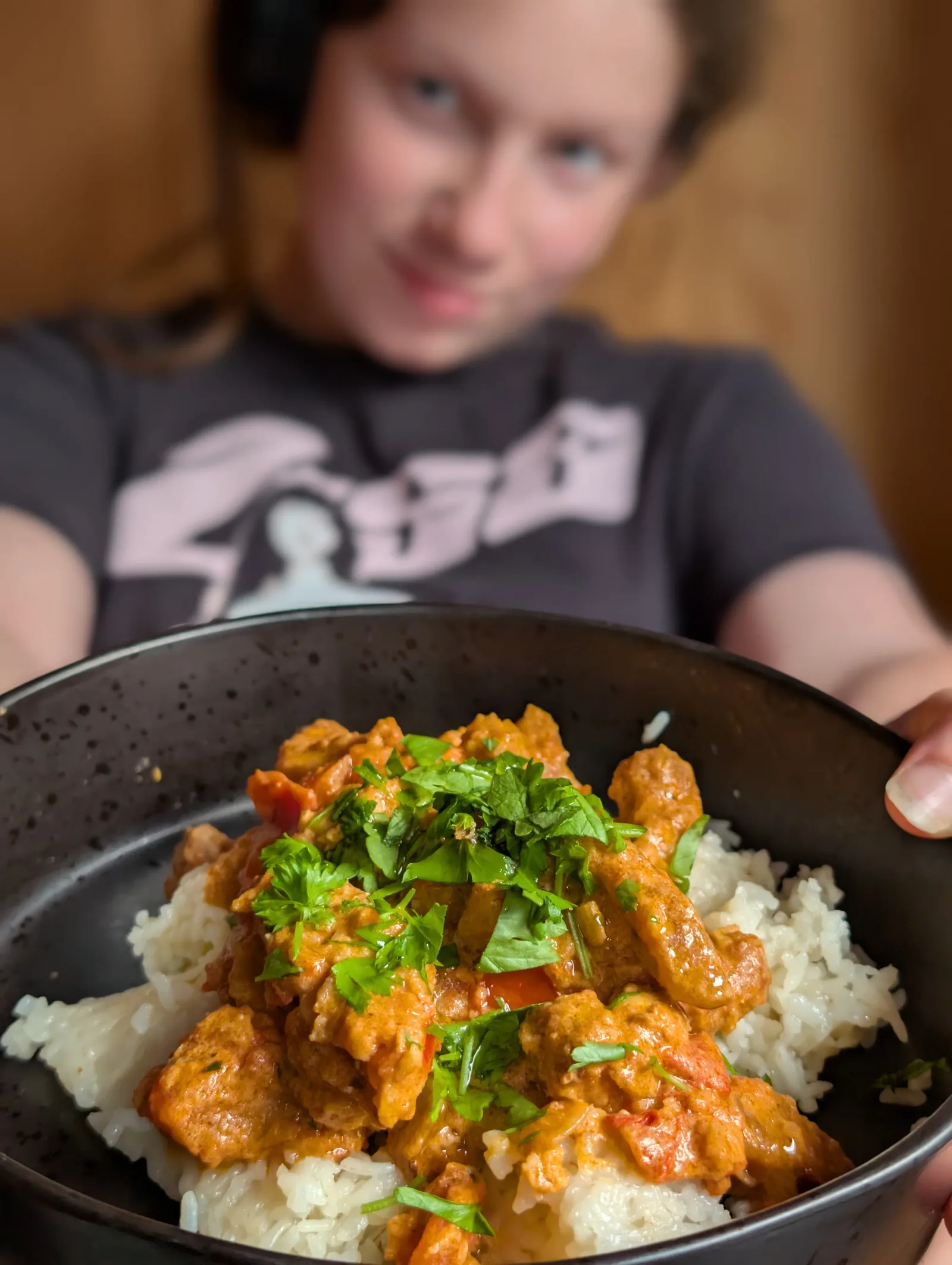A black bowl of chicken curry on white rice, topped with fresh parsley, held up to the camera