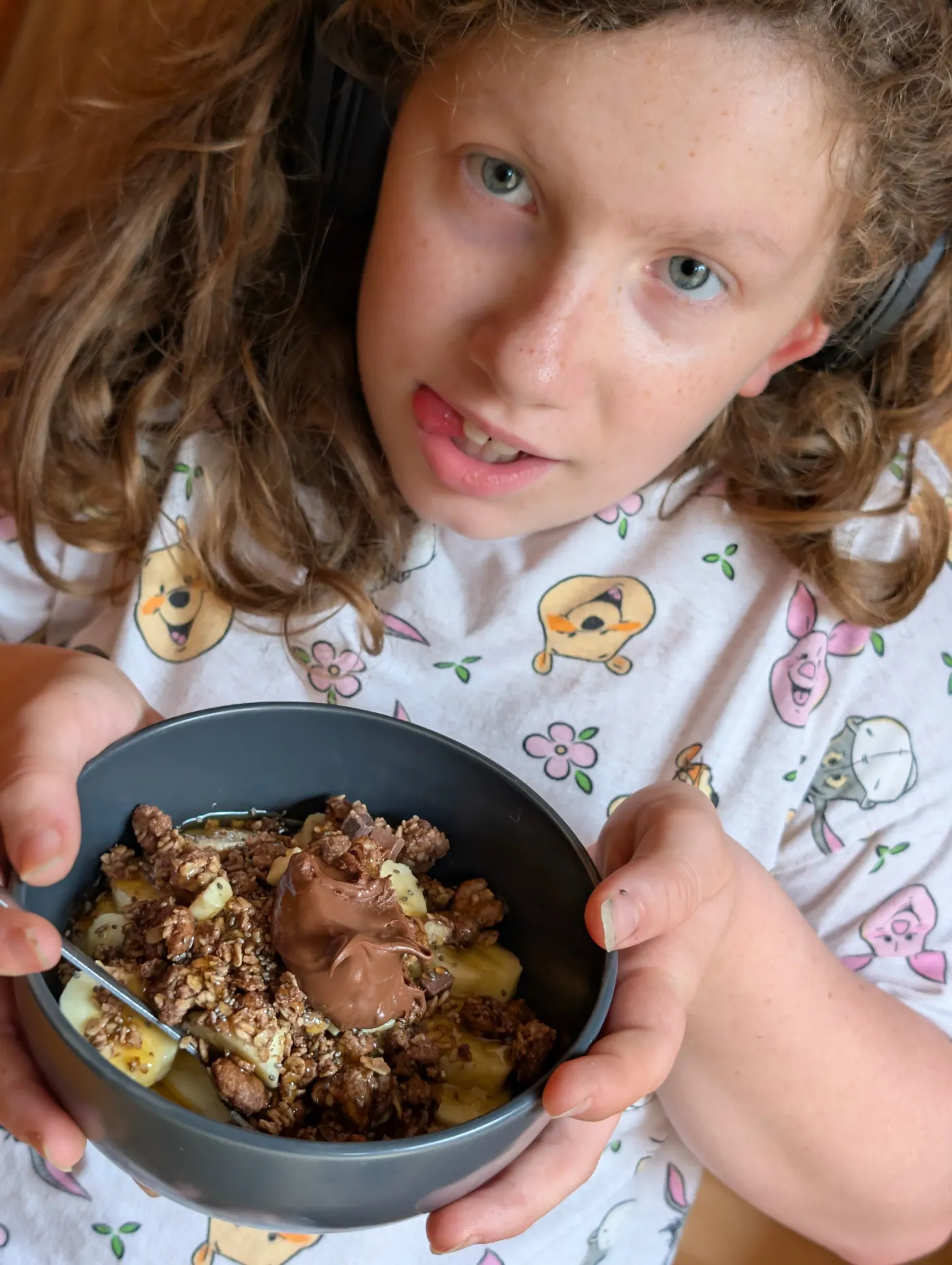 Ava holding up the finished bowl of yoghurt, banana and granola with a spoonful of Nutella on top
