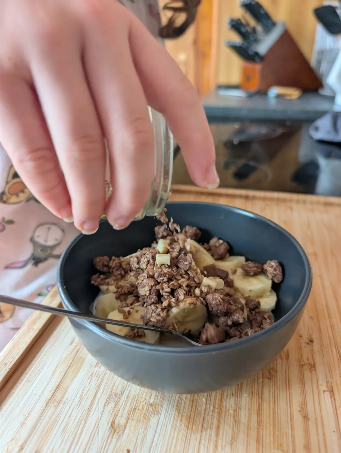 Granola being tipped from a glass jar over the sliced banana