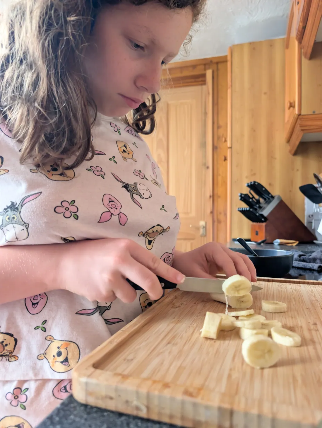Ava slicing a banana on a wooden board with a small knife