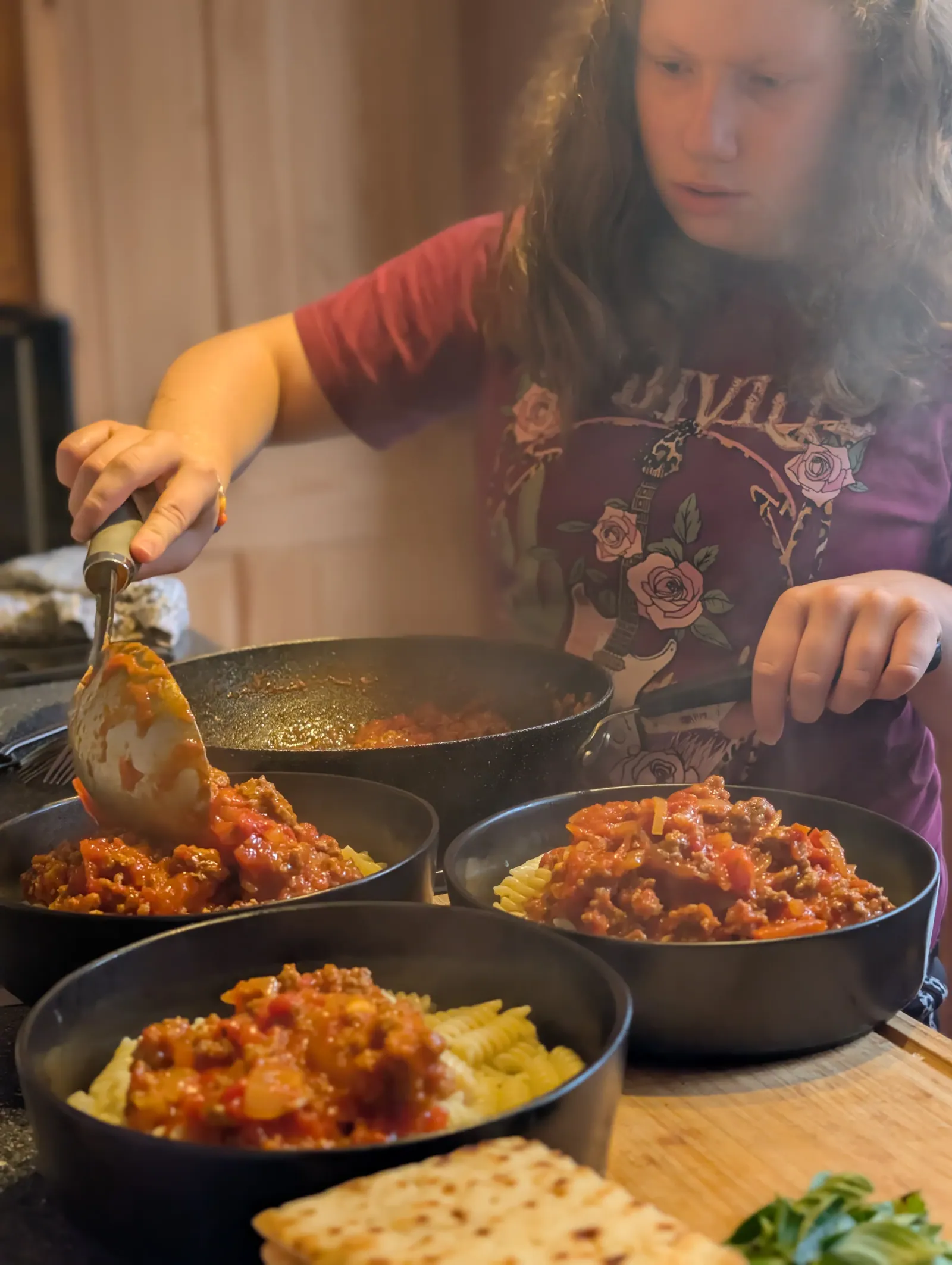 Ava spooning bolognese sauce over three bowls of pasta lined up on the worktop