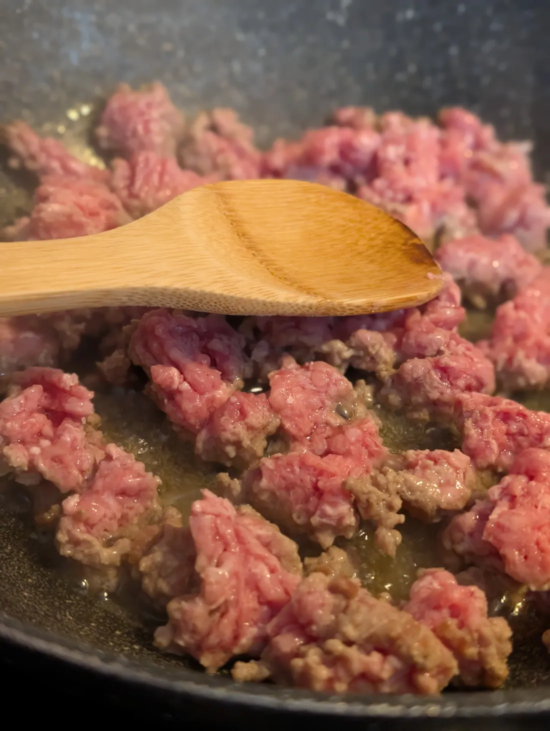 Minced beef browning in a pan with a wooden spoon