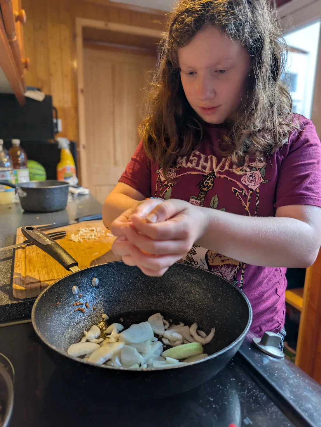 Ava dropping chopped garlic into a pan of sliced onions