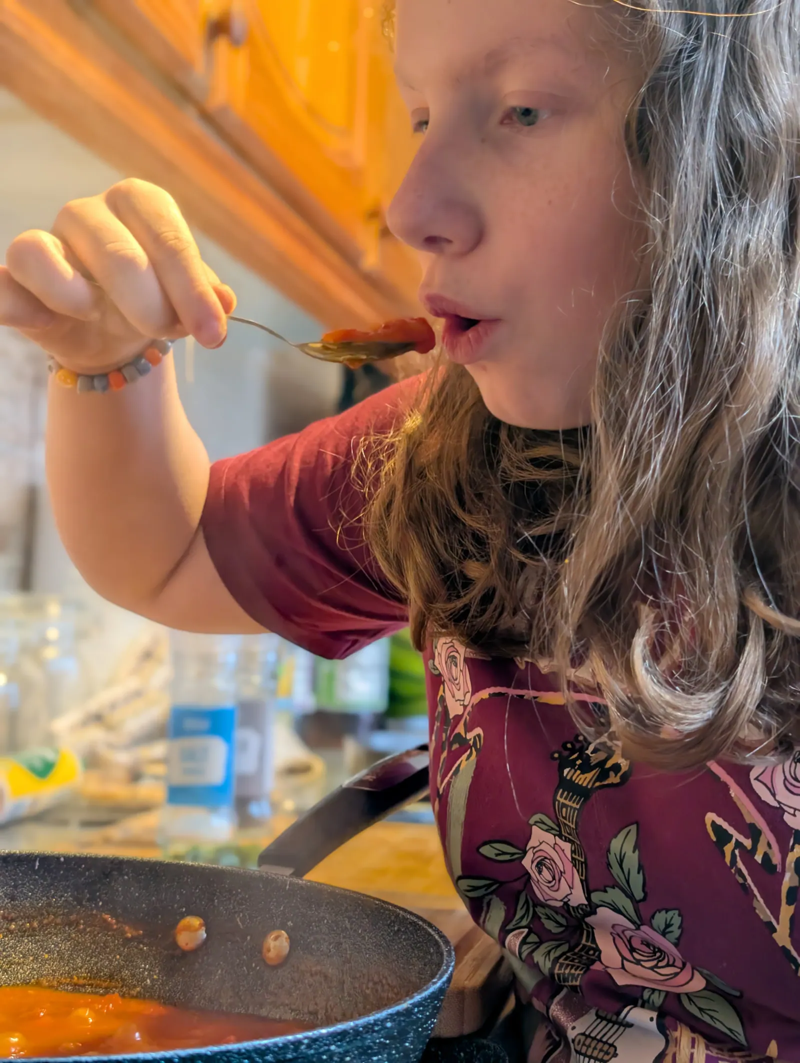 Ava tasting the sauce from a spoon over the pan