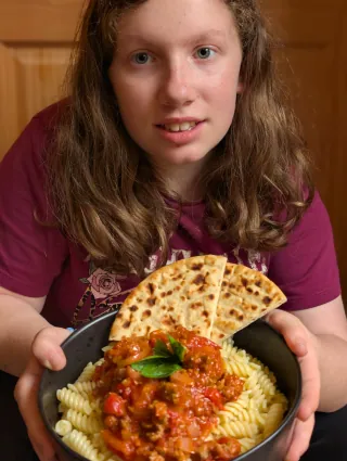 A bowl of pasta with bolognese, basil and flatbread