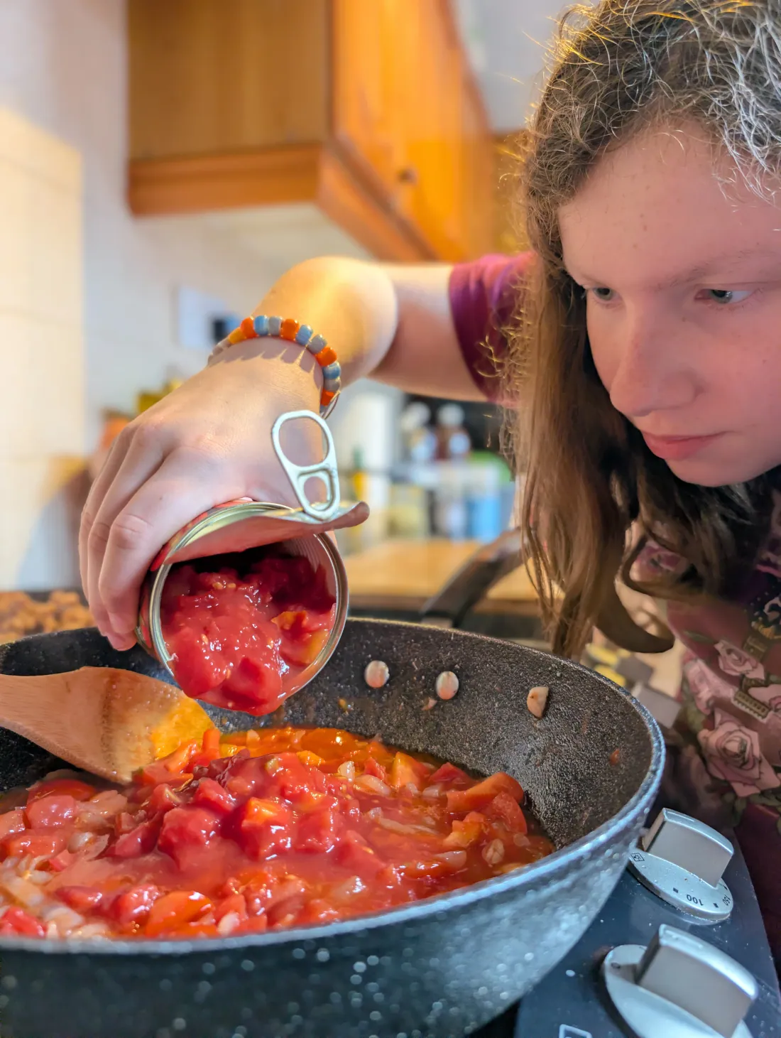 Ava tipping a tin of chopped tomatoes into the pan
